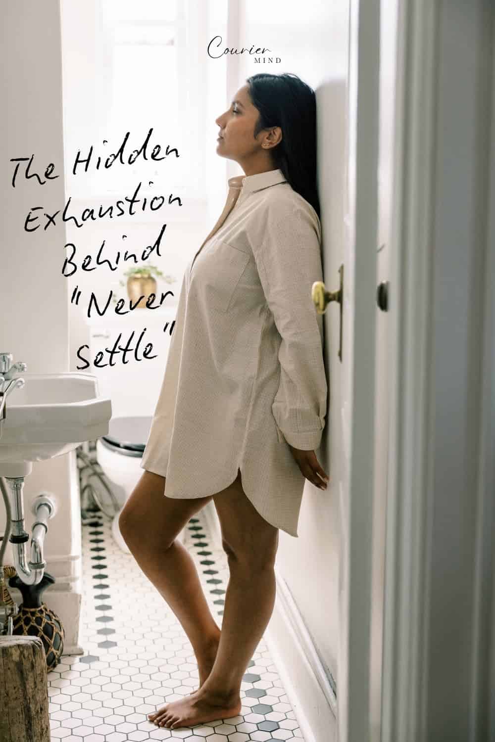Woman leaning against a bathroom wall wearing a loose, light-colored shirt dress.