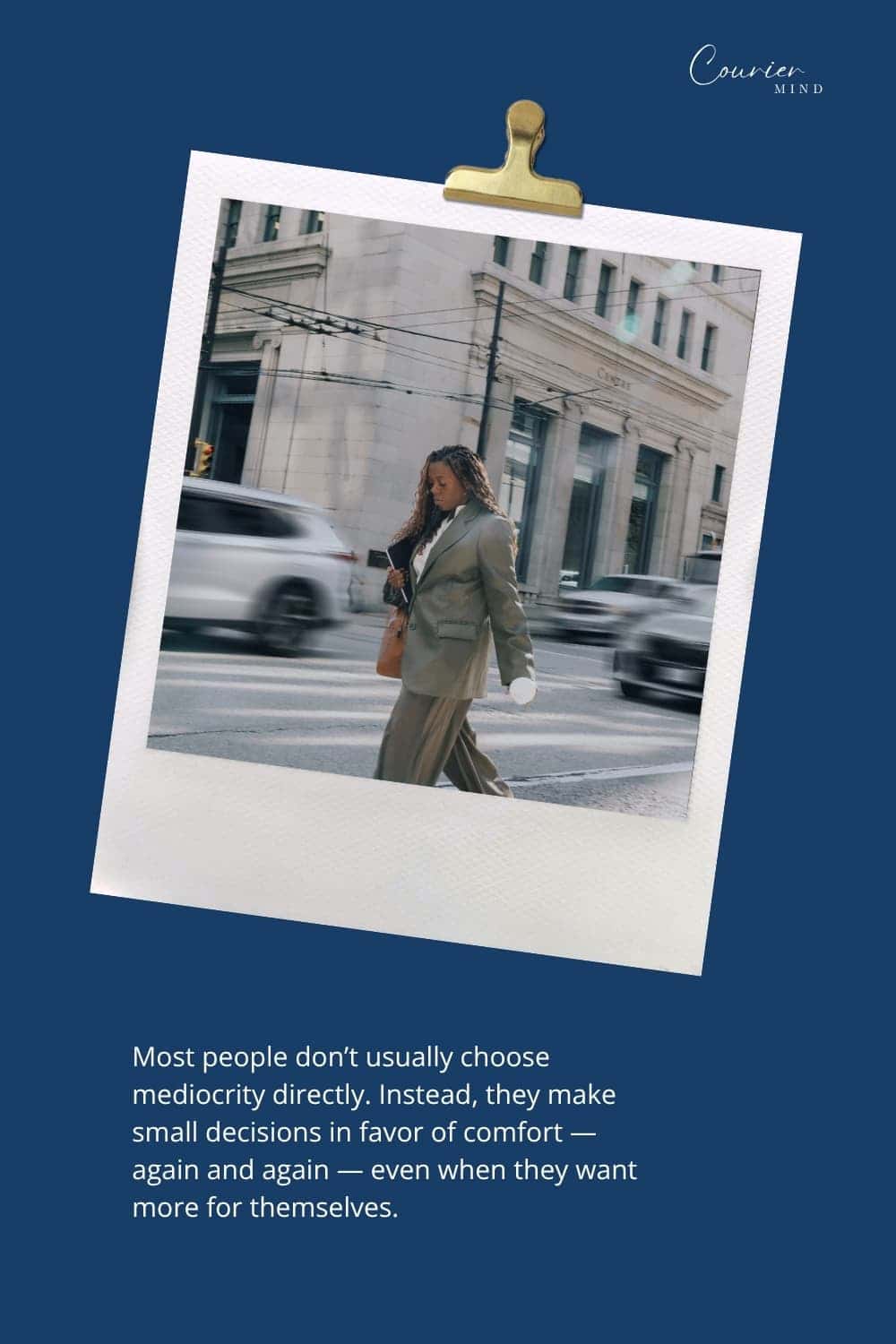 Woman in a business suit walking across a city street with her head down as cars blur past in the background.