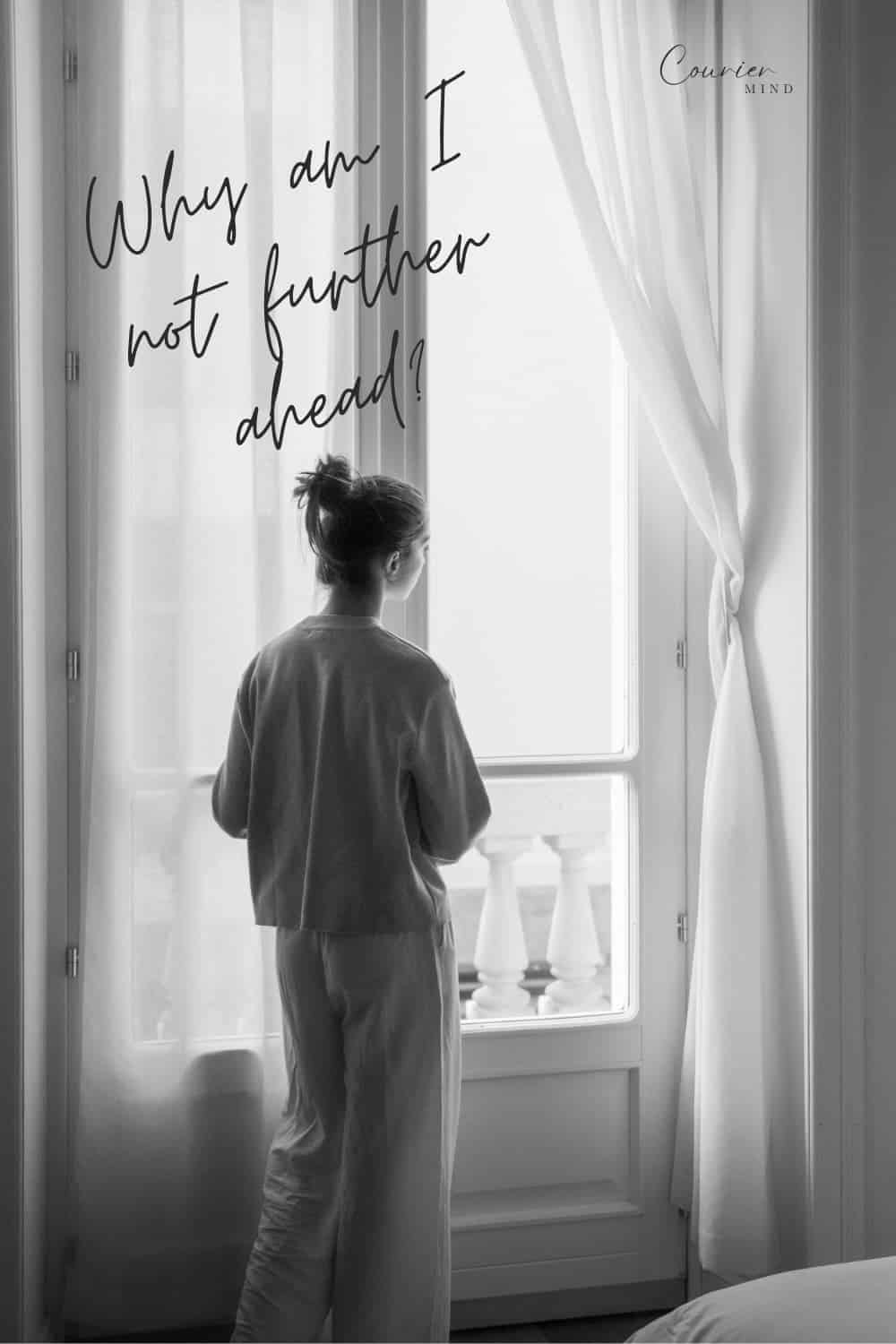Woman with her hair in a bun standing with her back to the viewer and looking out a large window.