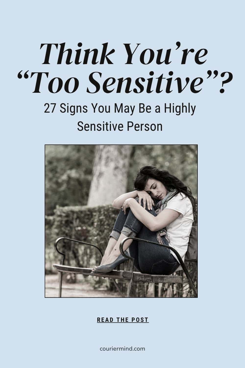 A woman sits on a park bench hugging her knees and looking sad.