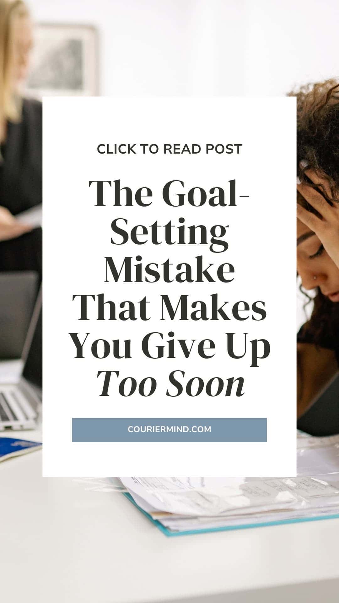 A woman sits at work looking down at documents in front of her, appearing tired.