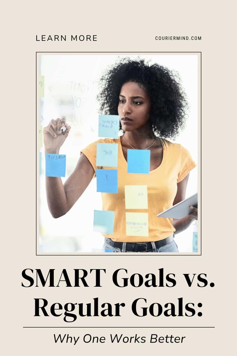 A woman with a large curly afro holds a tablet while standing in front of a glass board covered with sticky notes.