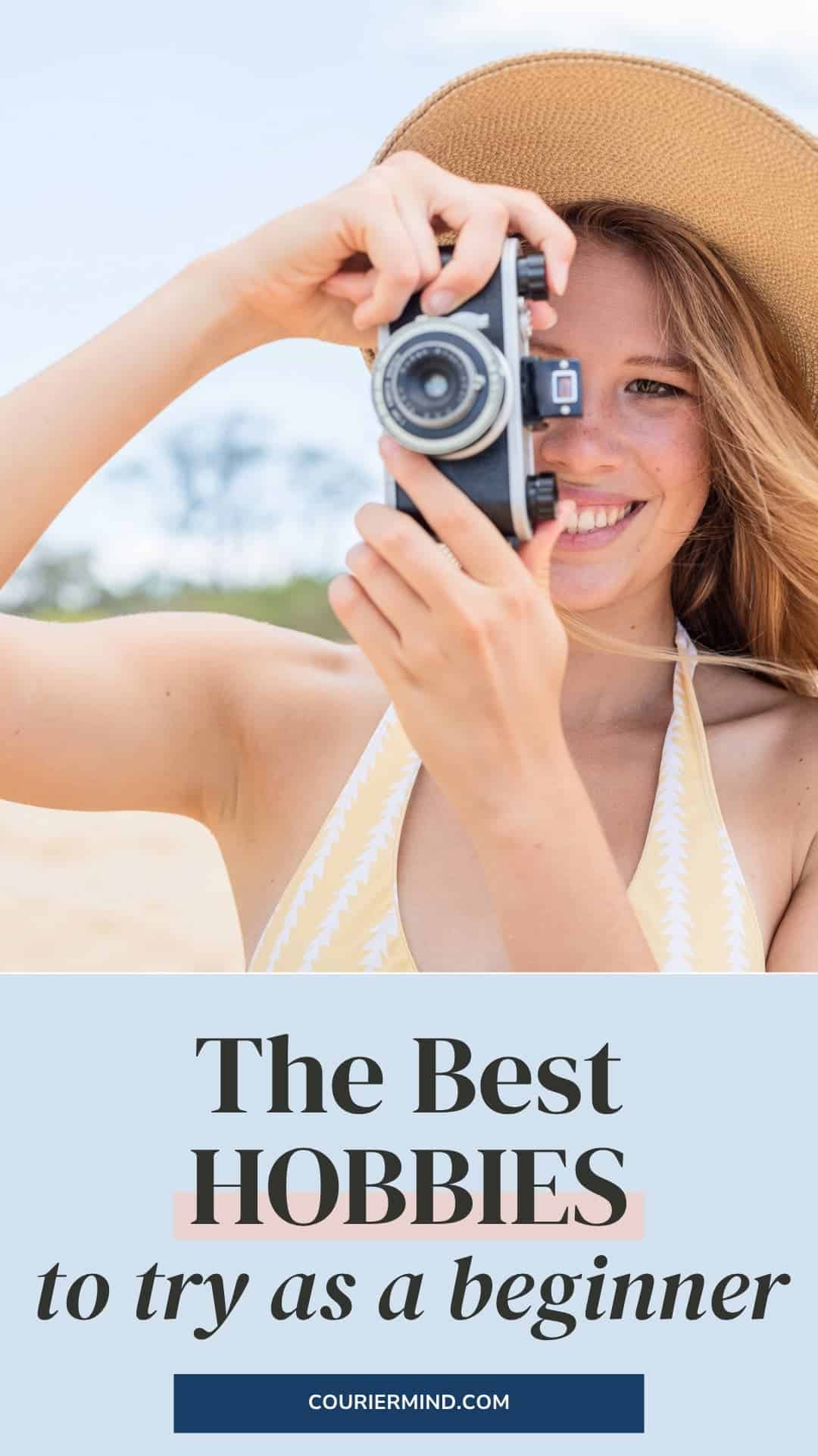 A woman at the beach holding a small blue camera up to her face, wearing a straw hat.