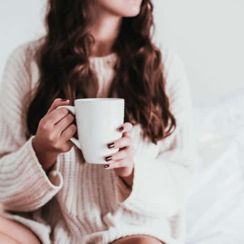 Woman relaxing in bed with a hot beverage.