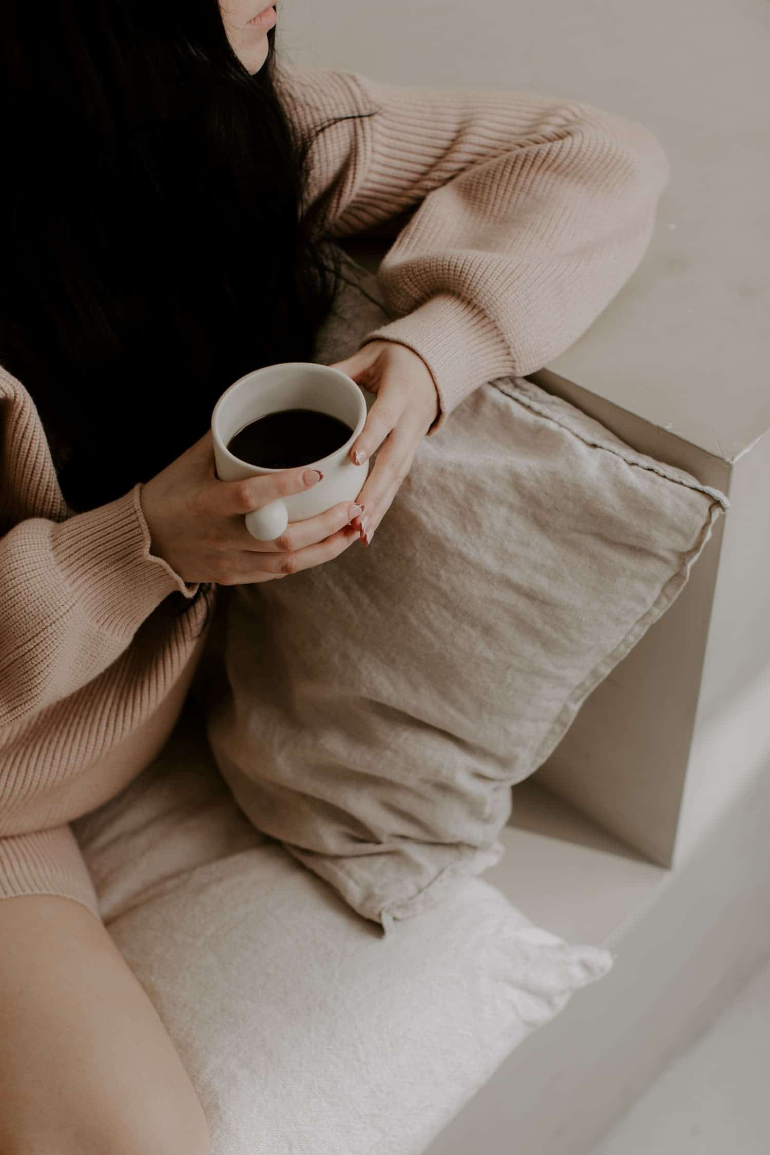 Woman lounging in pink cozy outfit while holding hot beverage.